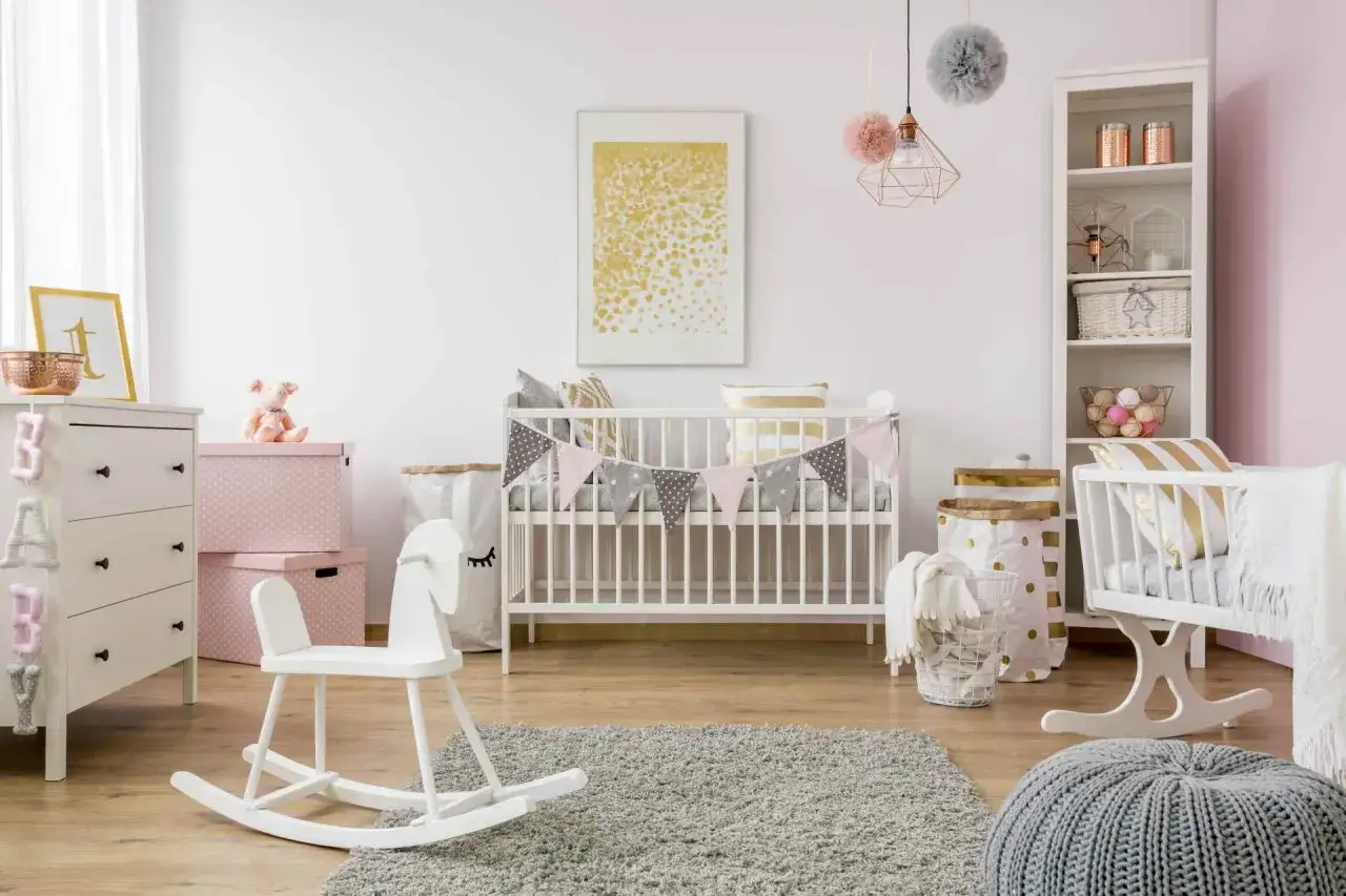 Cameretta neonato moderna con lettino, cassettiera, cavallo a dondolo e decorazioni in rosa e grigio.
