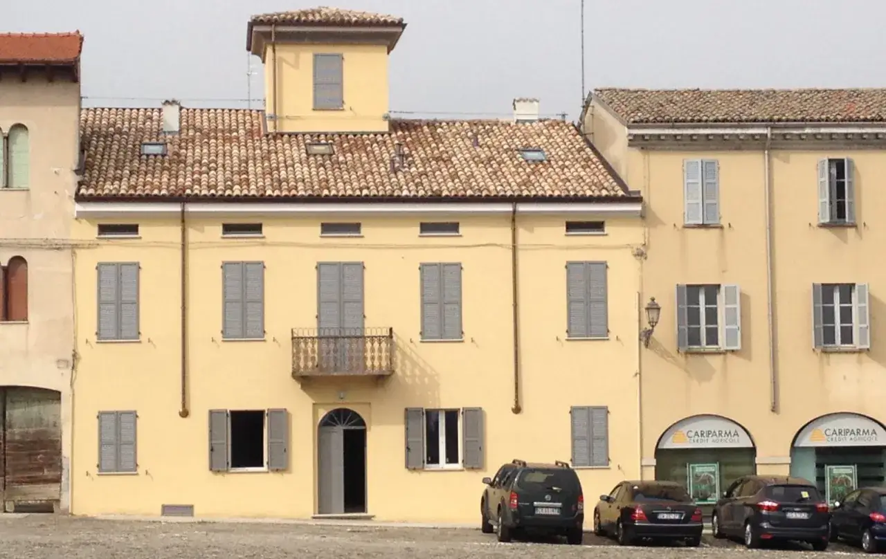Edificio giallo con intonachino silossanico, tegole rosse, persiane grigie e un piccolo balcone. Auto parcheggiate davanti.