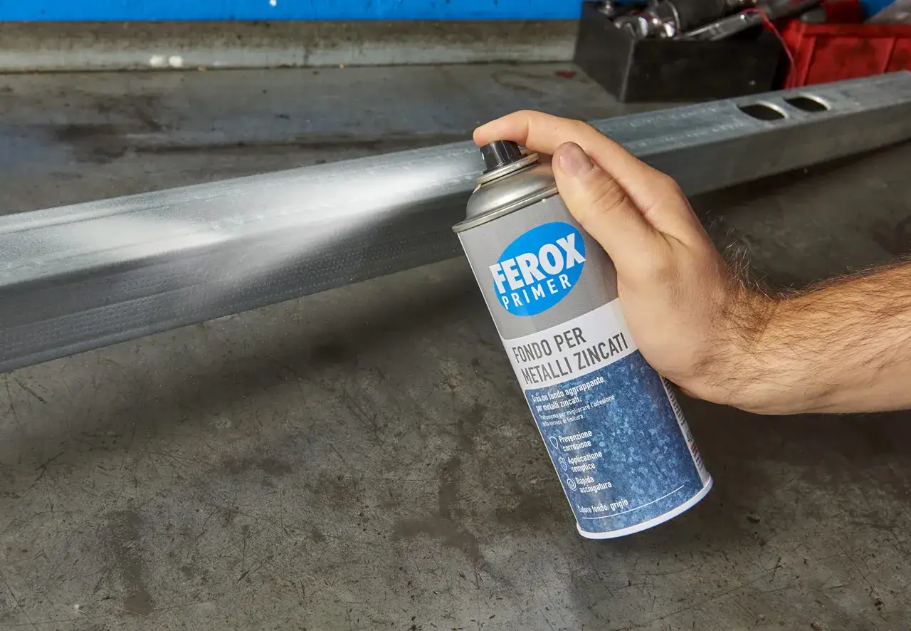 Mano spruzza primer Ferox su un profilo metallico zincato per migliorarne l'adesione.