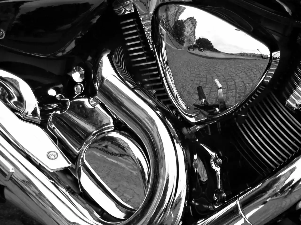 Dettaglio cromato di una moto, con riflessi di un palazzo e strada acciottolata. Si può verniciare sopra il cromato per un look personalizzato.