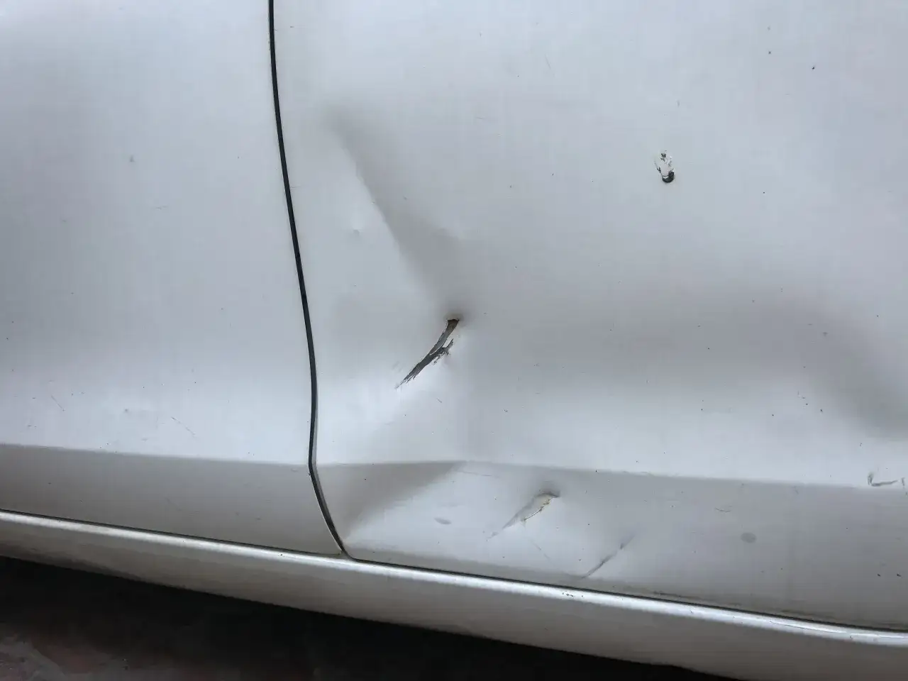 Portiera bianca con ammaccature e graffi, necessita di riparare carrozzeria.