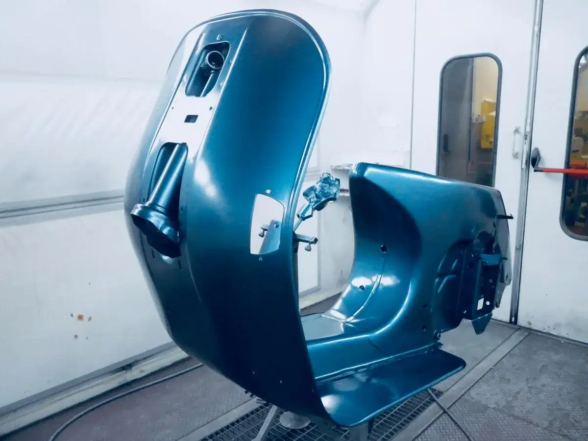 Parti di una Vespa appena verniciate in un blu metallizzato brillante, pronte per essere rimontate. Un lavoro di verniciare Vespa senza sabbiare, per un risultato impeccabile.