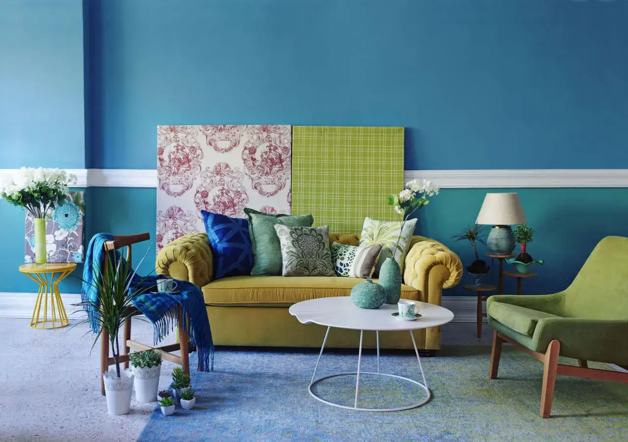 Salotto con divano giallo, cuscini colorati e pareti blu. Un tocco di creatività con pannelli decorativi, ispirazione per vernici fai da te.