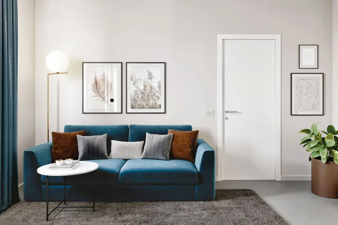 Divano blu intenso con cuscini tortora e grigi, un tavolino bianco e un tappeto scuro creano un elegante abbinamento color tortora e blu.
