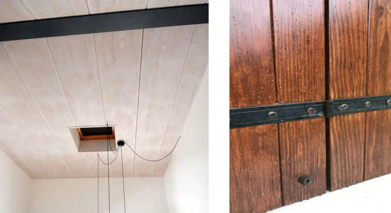Soffitto in legno sbiancato con trave nera e botola. Porta in legno scuro con cerniere metalliche, il mordente significato è la profondità del colore.