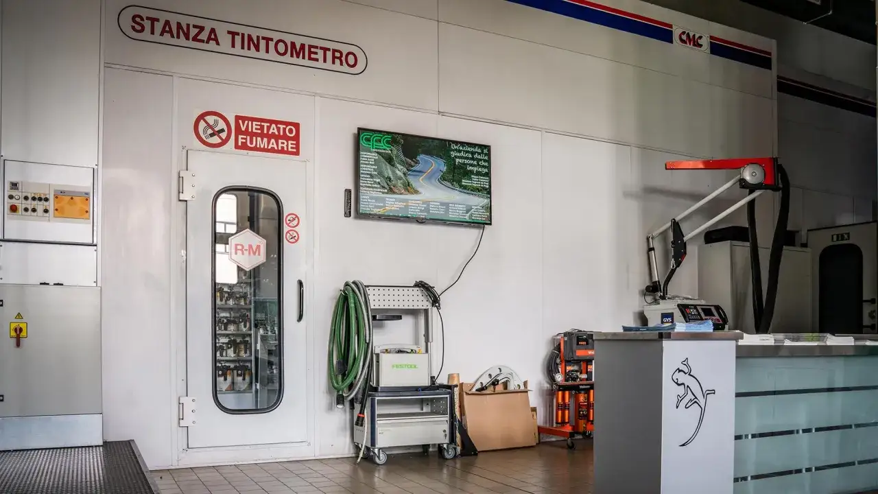 Stanza tintometro con attrezzature per la verniciatura e un monitor che mostra un'azienda.