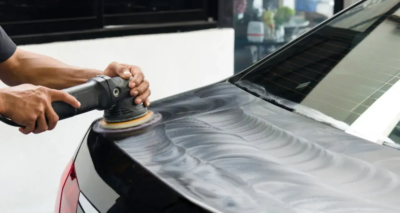 Mani che lucidano la carrozzeria di un'auto nera con una lucidatrice, un perfetto esempio di verniciare auto fai da te per un risultato professionale.