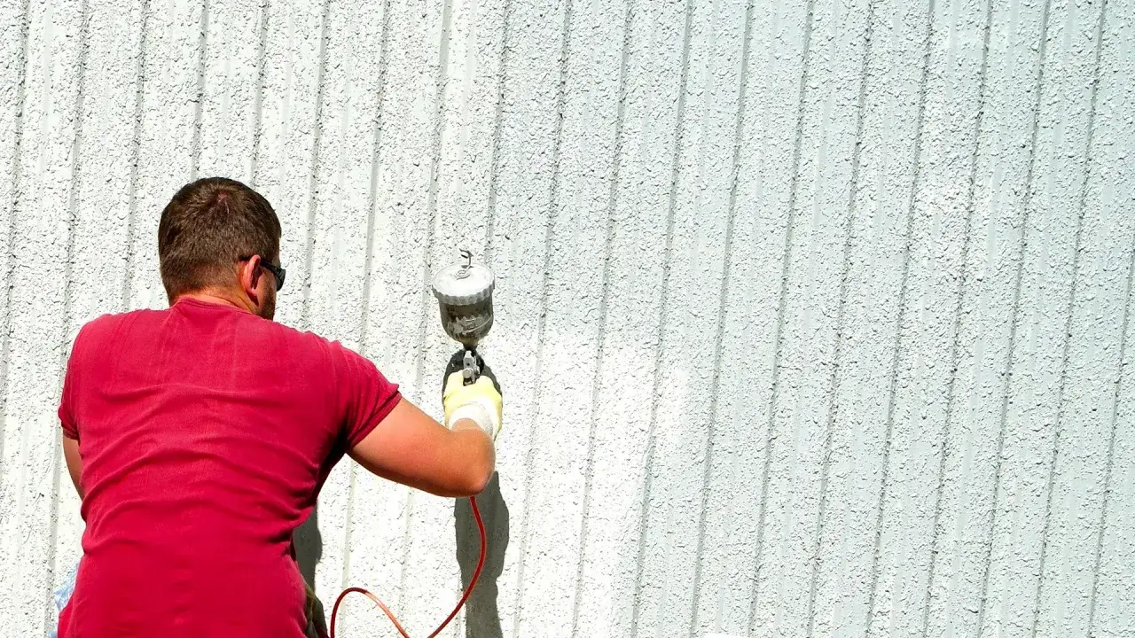 Uomo con maglietta rossa esegue la diluizione pittura murale a spruzzo su una parete esterna.