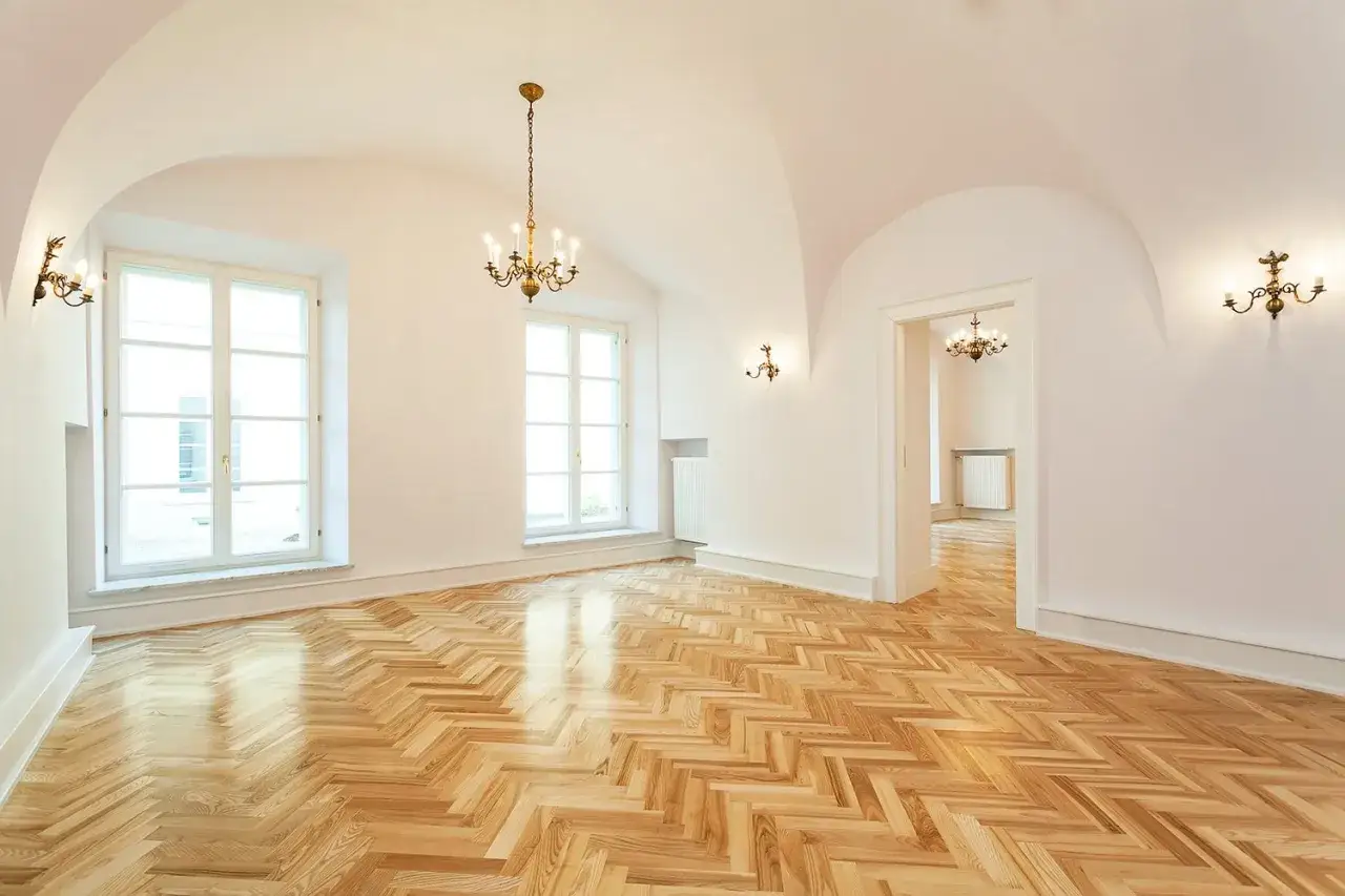 Luminosa stanza con soffitto a volta, parquet a spina di pesce e finitura satinato. Due grandi finestre e un'apertura su un'altra stanza.