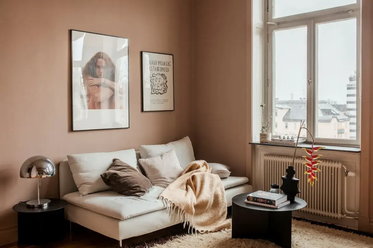 Un accogliente salotto con divano bianco, coperte morbide e quadri alle pareti color tortora rosato.