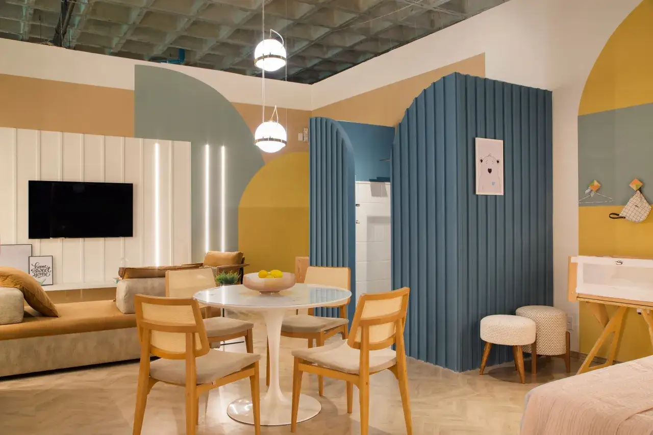 Un soggiorno moderno con divano color ocra, tavolo rotondo, sedie in legno e pareti decorate con forme geometriche e colori vivaci.