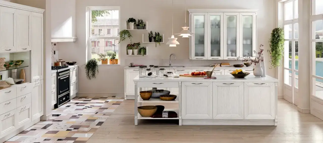 Cucina luminosa con mobili bianchi decapato, isola centrale, fornelli neri e pavimento geometrico.