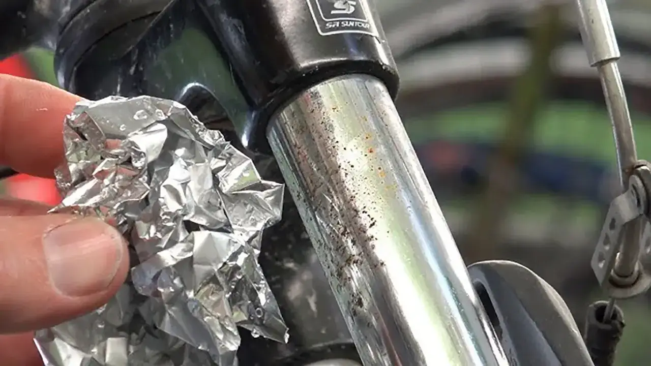 Mano con foglio d'alluminio vicino a stelo forcella bicicletta con cromatura rovinata e macchie di ruggine.