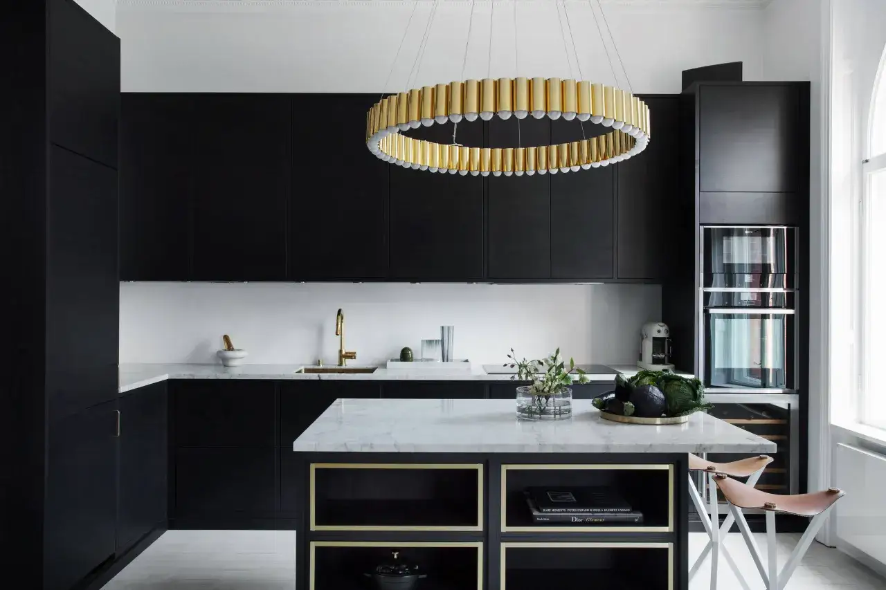 Cucina nera con pareti bianche, isola in marmo e lampadario dorato.