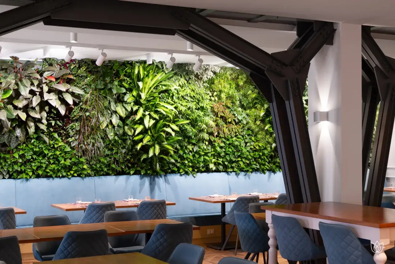 Interno di un ristorante con parete verde lussureggiante, sedute blu e tavoli in legno. Un vero stile urban jungle.