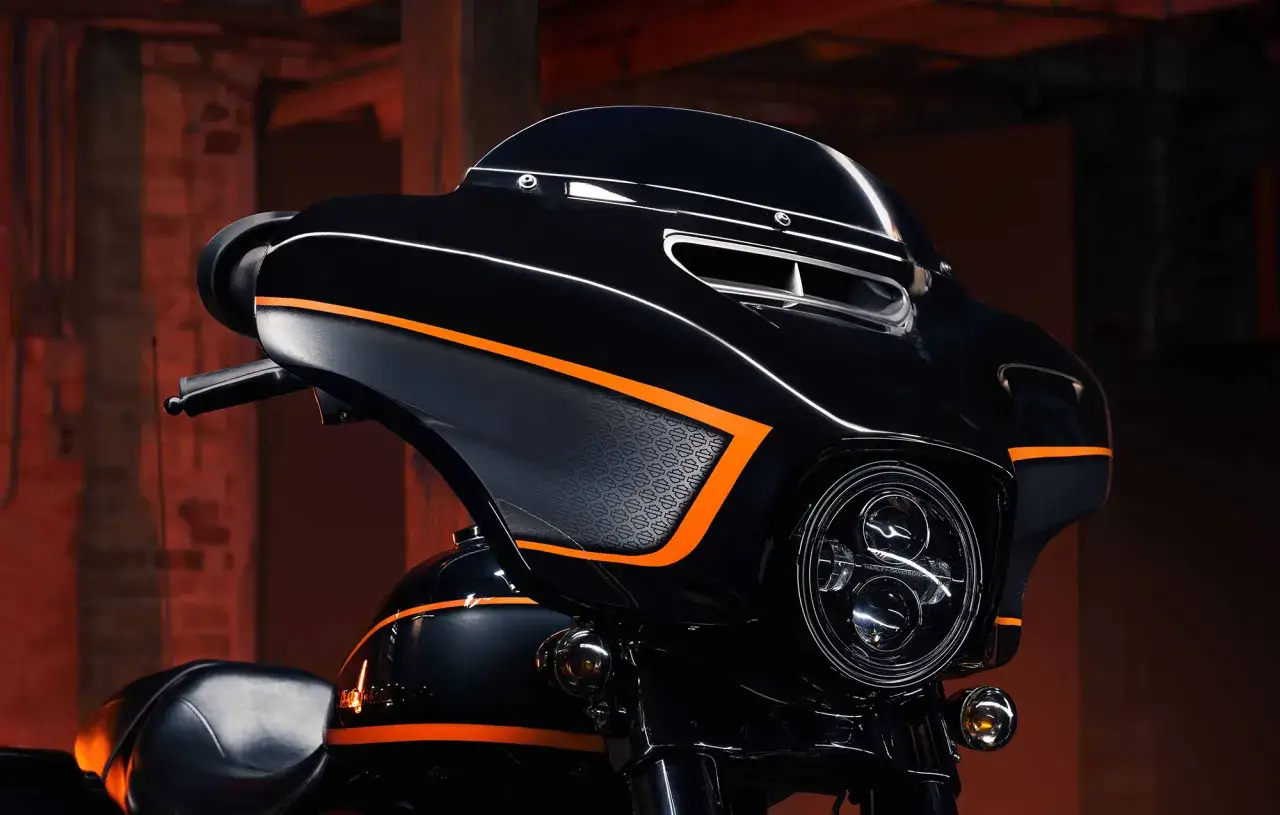 Dettaglio di una moto Harley-Davidson nera con accenti arancioni vivaci. I colori Harley-Davidson risaltano sul cupolino e sul serbatoio.