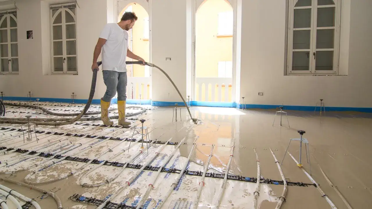 Operaio versa cemento e acqua senza sabbia su un massetto con riscaldamento a pavimento.