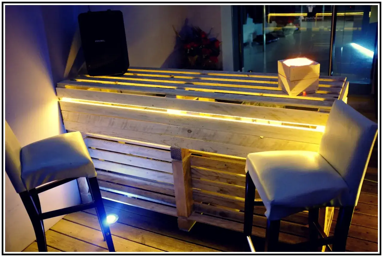 Bancone bar fai da te con pallet, illuminazione a LED e sgabelli. Un'idea creativa per un angolo bar moderno e accogliente.