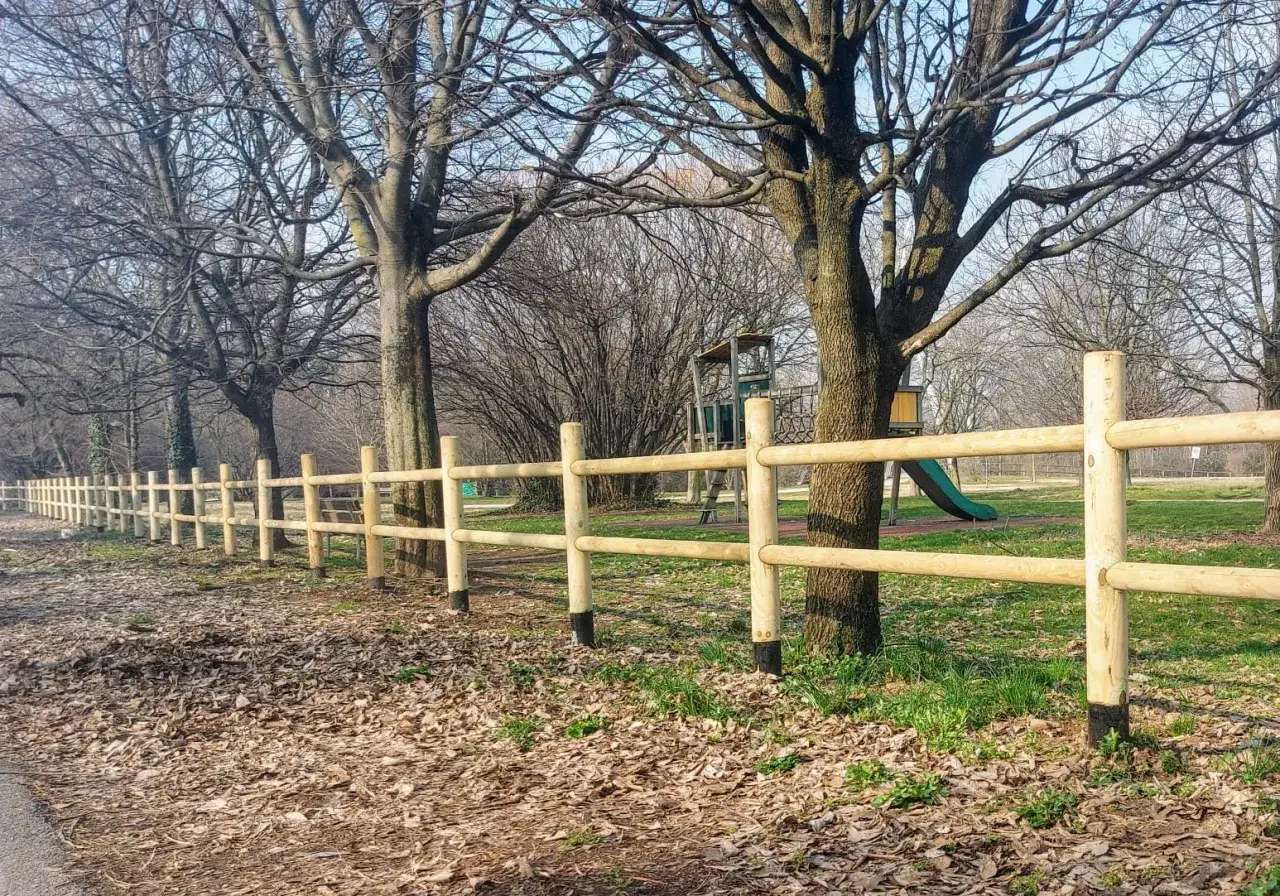Nuova staccionata in legno fai da te delimita un'area verde con alberi spogli e un parco giochi sullo sfondo.