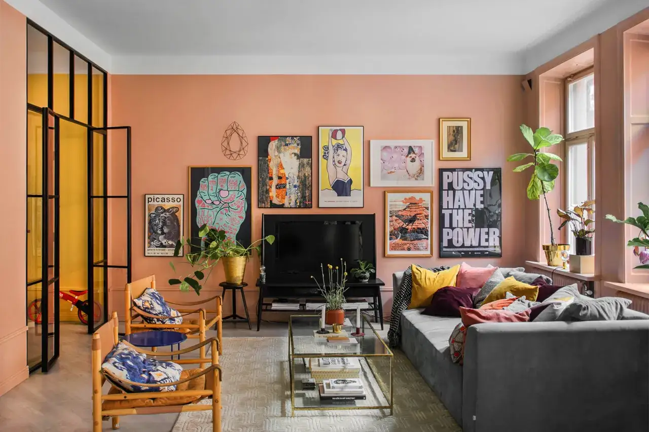 Salotto con pareti color rosa pesca, divano grigio, quadri pop e un tavolino di cristallo.