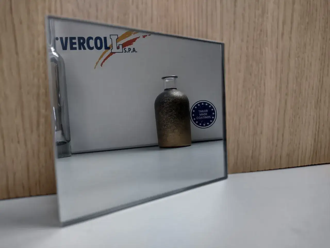 Bottiglia riflette su specchio con logo Vercol. Il cromato significato è la lucentezza che cattura la luce.