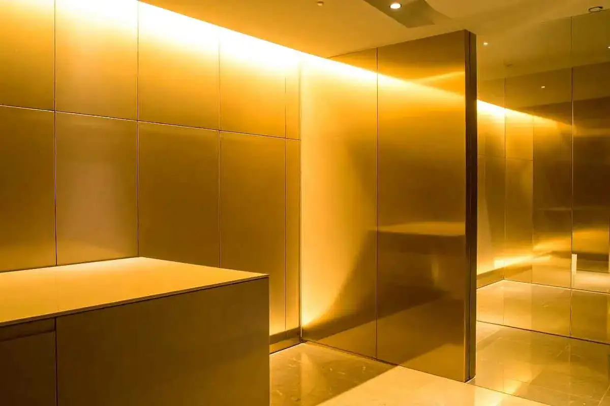Un corridoio moderno con pareti e soffitto in un caldo colore dorato, illuminato da luci soffuse che creano riflessi lussuosi.