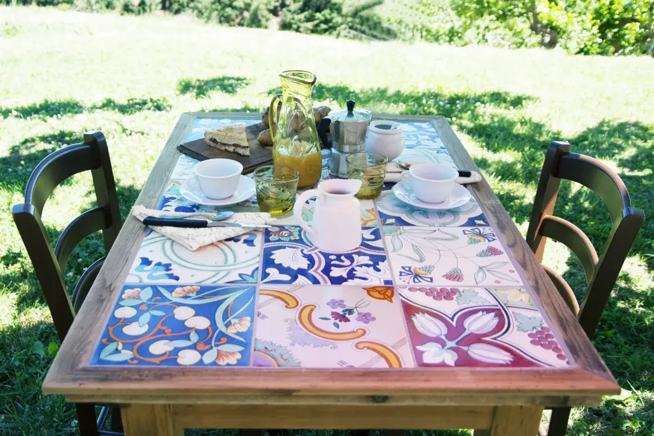 Tavolo con piastrelle fai da te, perfetto per un brunch all'aperto. Colori vivaci e motivi floreali creano un'atmosfera gioiosa.