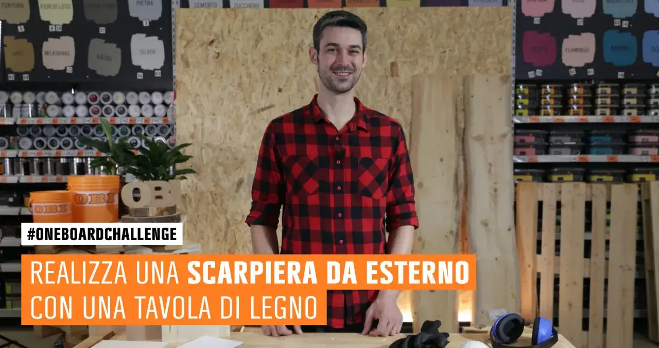 Uomo con camicia a quadri rossi presenta un progetto di scarpiera fai da te legno, con attrezzi e materiali da bricolage sullo sfondo.