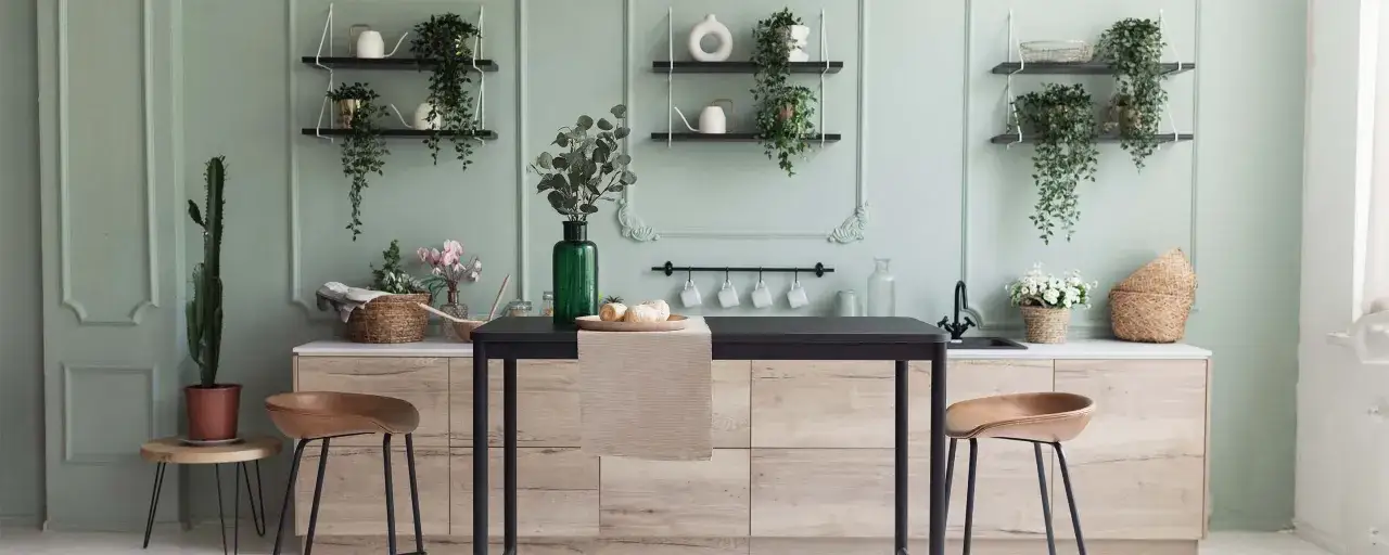Cucina moderna con pareti verde salvia, isola centrale con sgabelli in pelle, piante e decorazioni in vimini.