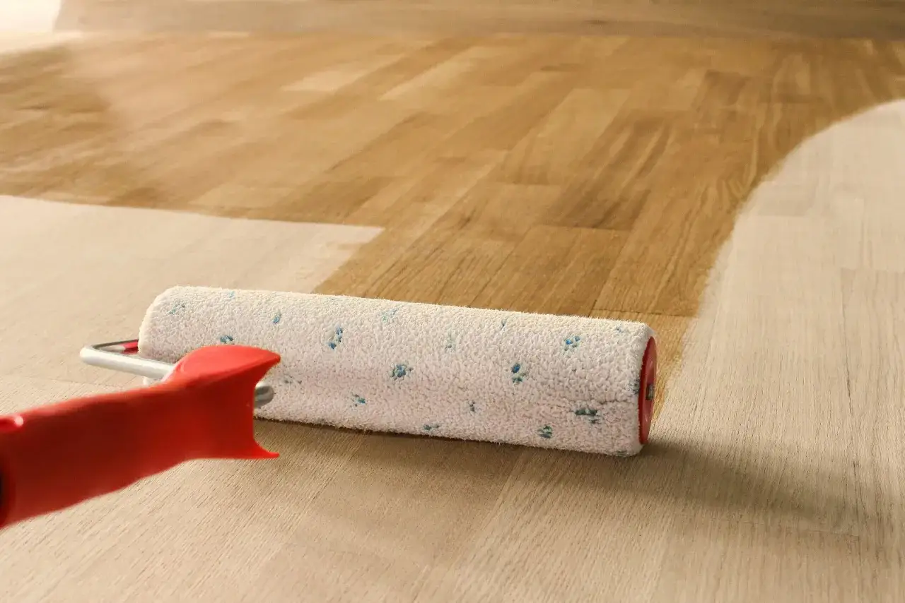 Rullo applica verniciatura poliuretanica su parquet. La finitura lucida protegge il legno.