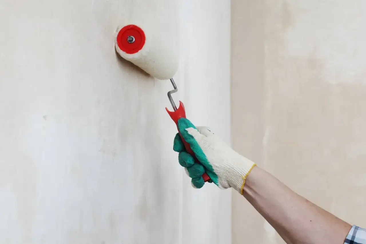 Mano guantata stende un undercoat bianco su un muro grezzo con un rullo da pittura.