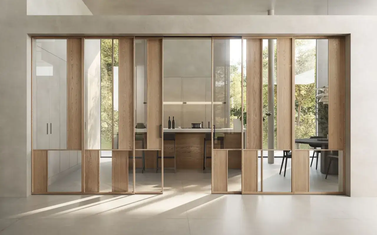 Porta scorrevole in legno e vetro, con un design che evoca lo stile brutalista nella sua essenzialit&agrave; materica, apre su una cucina moderna.