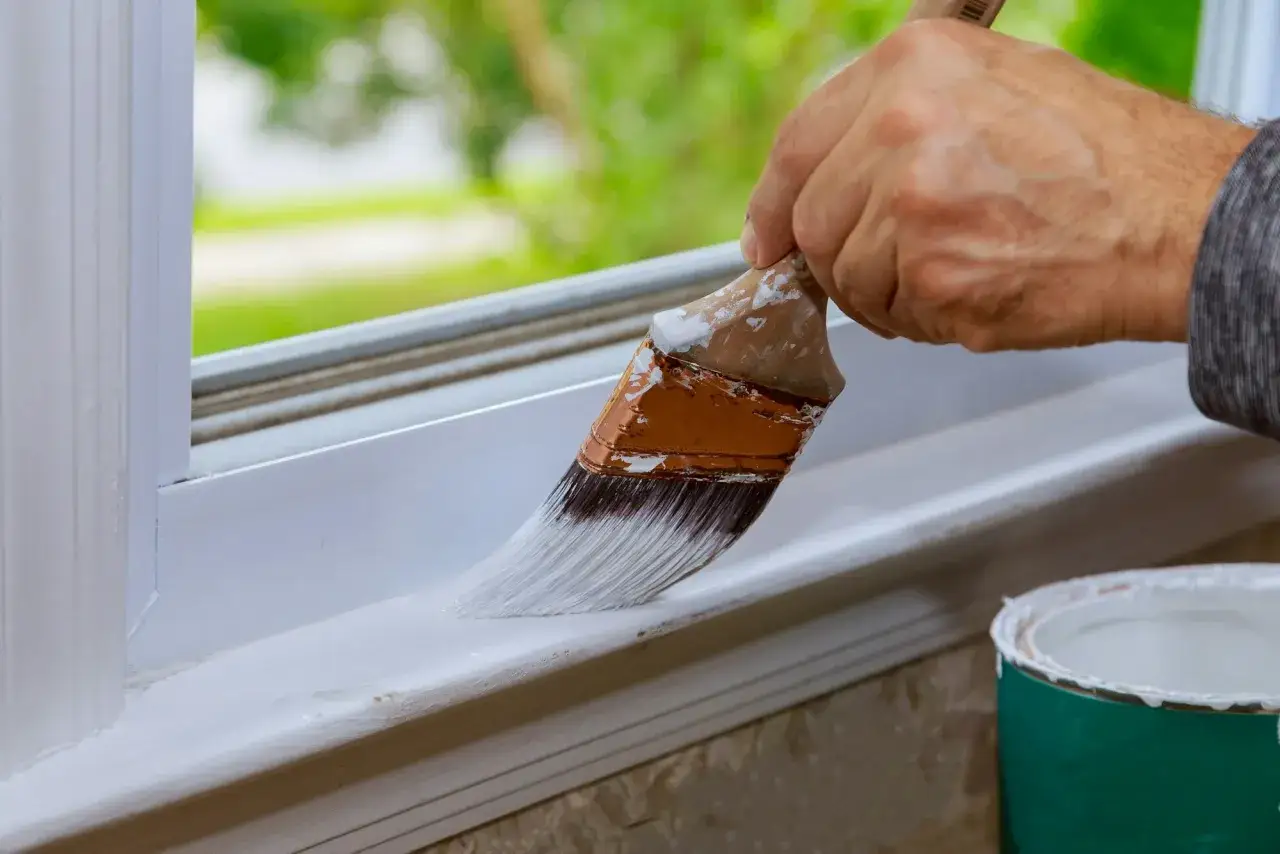Verniciatura infissi in legno esterni: una mano esperta rinnova il davanzale con pittura bianca.