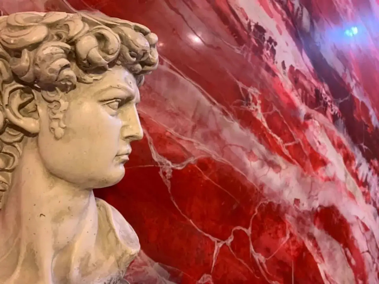 Busto classico in primo piano, con uno sfondo vibrante di pittura decorativa effetto marmo rosso e bianco.
