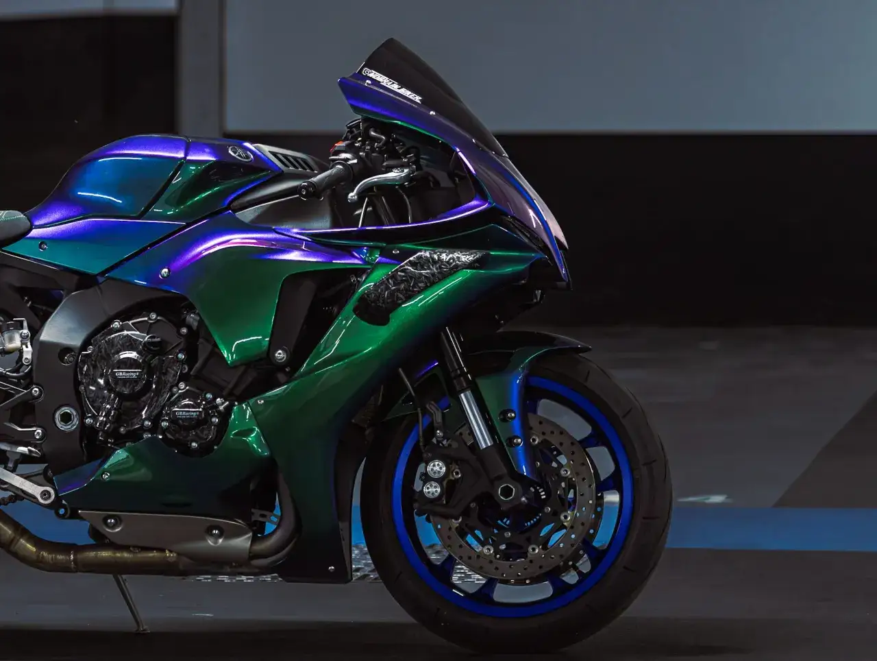 Moto sportiva con vernice camaleonte che cambia colore tra blu e verde smeraldo, con dettagli in carbonio e cerchi blu.