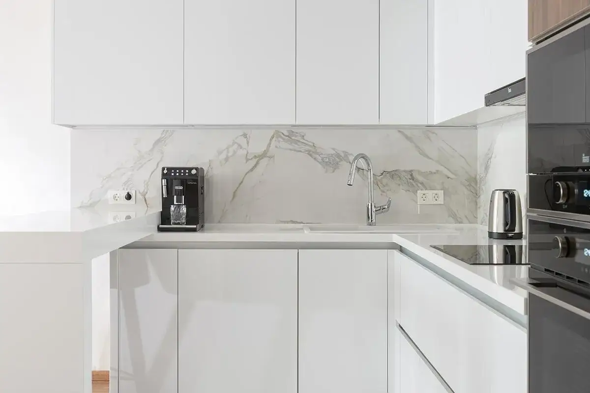 Cucina moderna con ante bianco lucido e piano in marmo. La differenza tra bianco lucido o opaco è evidente nei mobili.