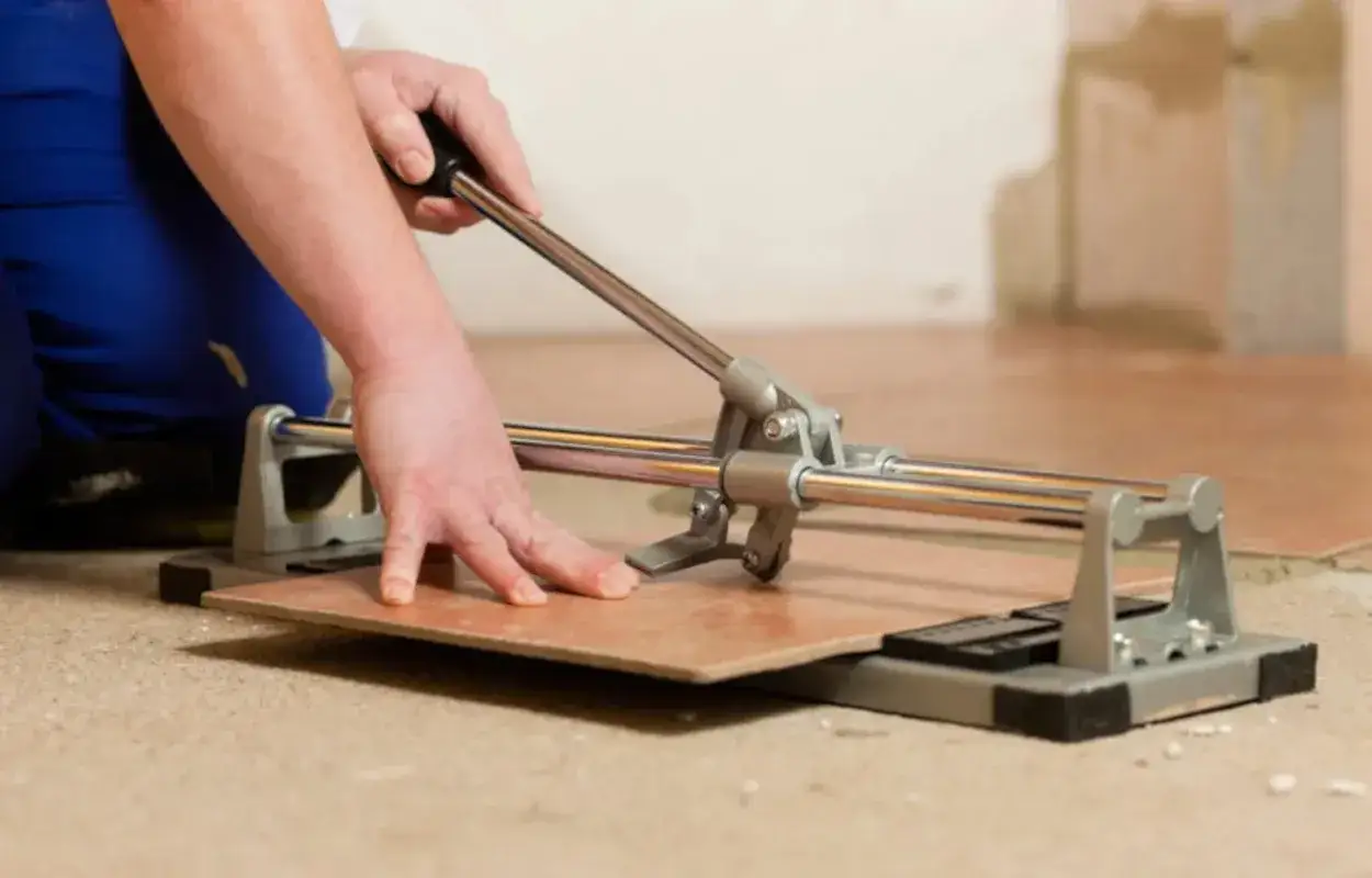 Mani esperte utilizzano un tagliapiastrelle per tagliare piastrelle a mano, creando un taglio preciso per la posa.