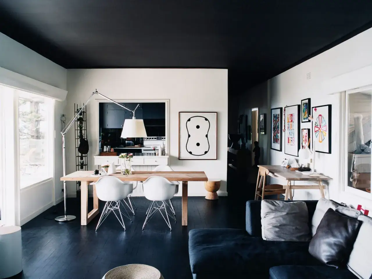 Un soggiorno moderno con soffitti colorati di nero intenso, un tavolo da pranzo in legno e sedie bianche, e un divano scuro.