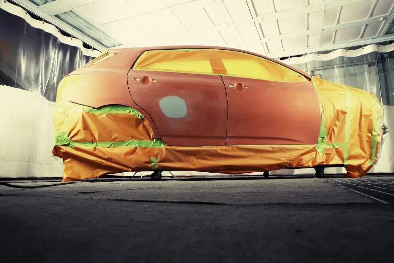 Auto in carrozzeria, pronta per verniciare con bomboletta. Finestrini coperti, carrozzeria arancione.