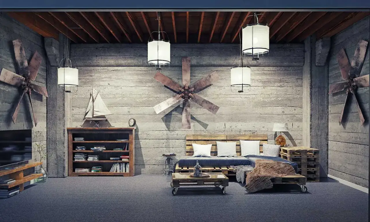 Salotto con divano e tavolino realizzati con riciclo pallet. Pareti in cemento grezzo, ventilatori industriali e illuminazione soffusa creano un'atmosfera unica.