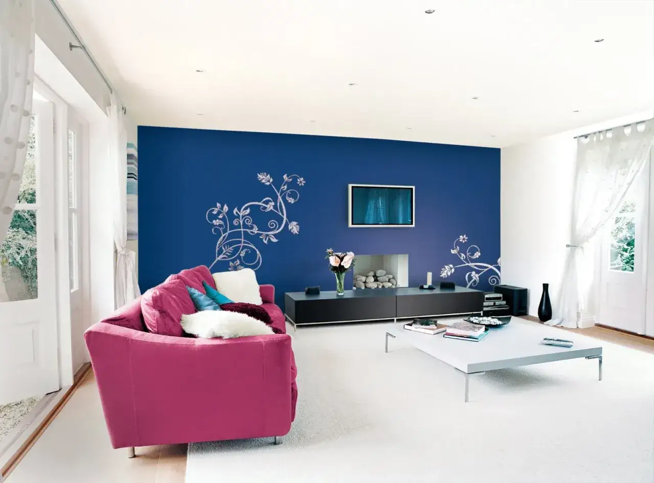 Soggiorno moderno con divano fucsia e parete blu con decorazioni floreali. Meglio vernice opaca o lucida? La finitura opaca della parete blu esalta le decorazioni.
