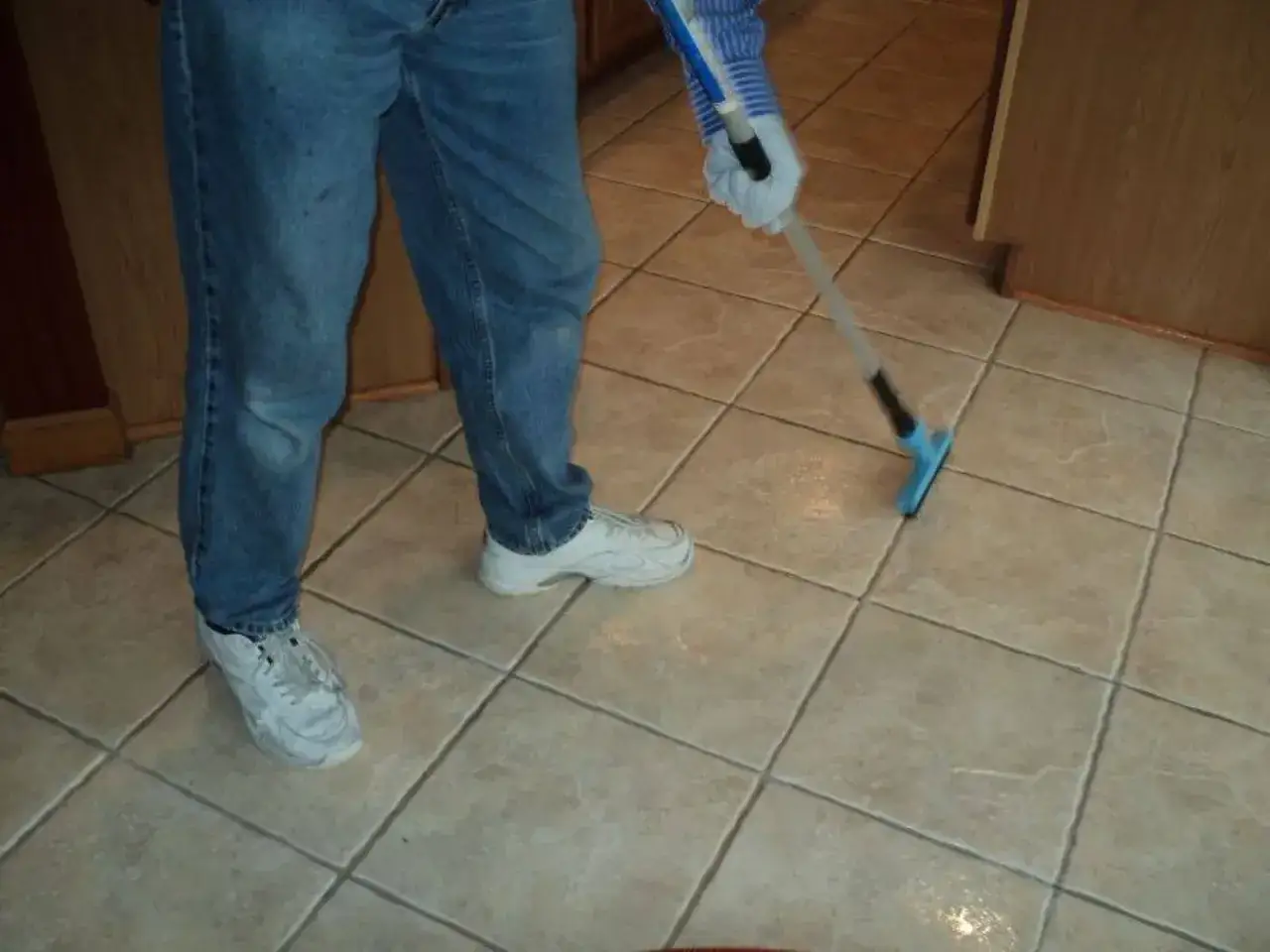 Persona con guanti e jeans pulisce le fughe del pavimento con uno strumento apposito.