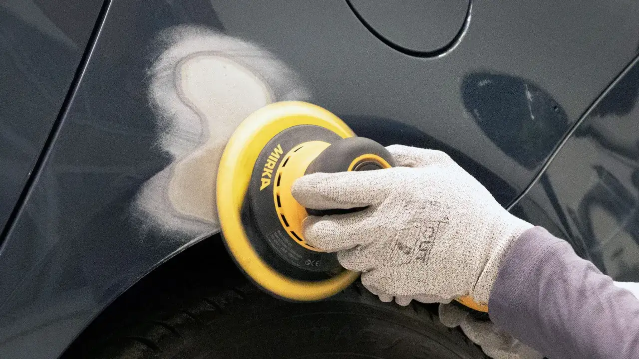 Utilizzo di una levigatrice orbitale per rimuovere vernice spray da carrozzeria, preparando la superficie per la riparazione.