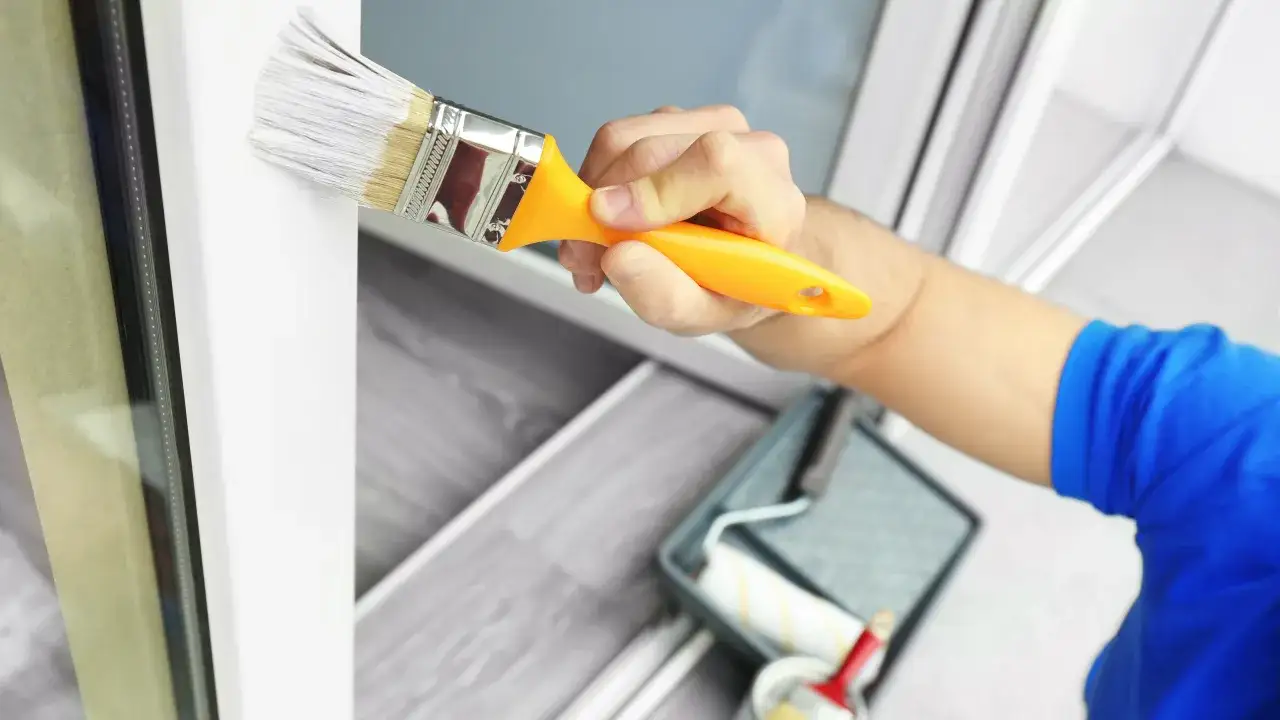 Mano che dipinge con un pennello bianco su una cornice bianca, dimostrando che si può verniciare il PVC.