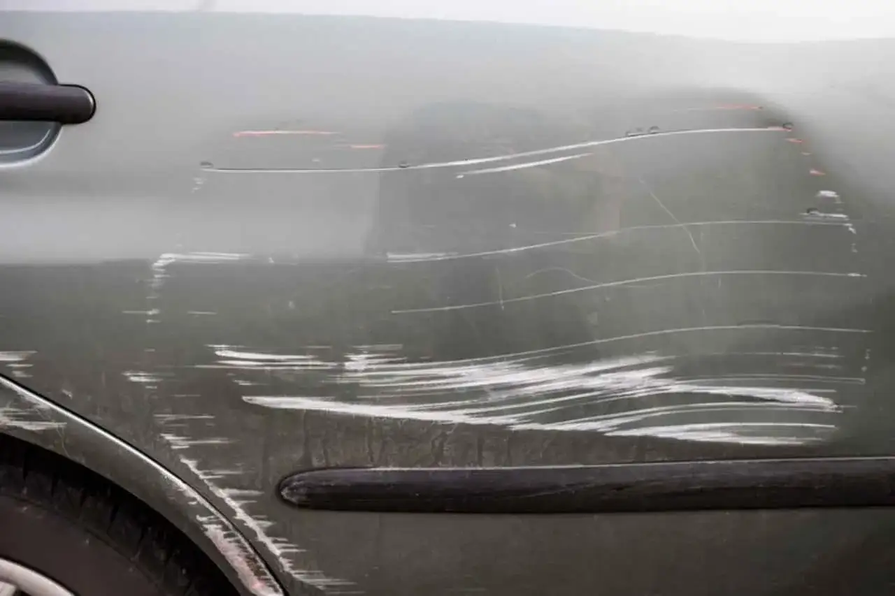 Dettaglio della portiera di un'auto con numerosi graffi superficiali e profondi, che illustrano diversi tipi di graffi auto.