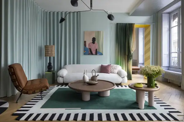 Salotto con divano bianco bouclé, poltrona in pelle, tappeto geometrico e lampada da terra, in un audace stile massimalista.