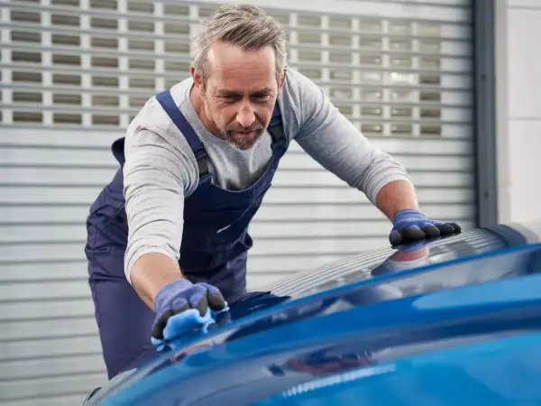 Un esperto opera la verniciatura auto con cura, lucidando la carrozzeria blu brillante.