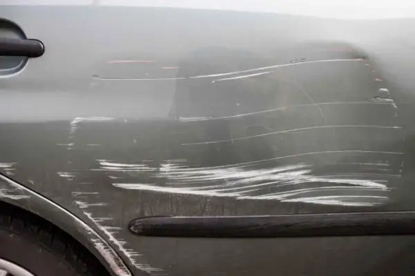 Dettaglio di una portiera d'auto con numerosi graffi superficiali e profondi, che illustrano vari tipi di graffi auto.