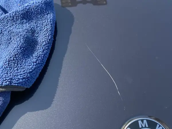 Un panno blu accanto a un graffio sulla vernice dell'auto, pronto per imparare come ritoccare vernice auto.