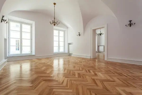 Un ampio salone con parquet a spina di pesce appena levigato, illuminato da grandi finestre e lampadari antichi.